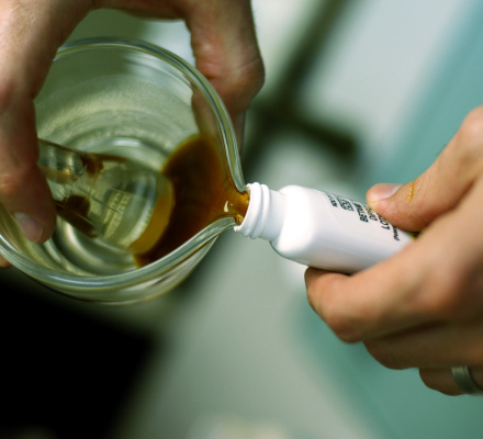 Brown liquid being poured from a measuring cup into a small bottle.
